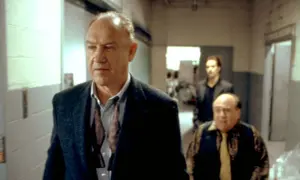 Gene Hackman in un film, cammina con altri due uomini in un corridoio.