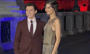 Tom Holland e Zendaya, una coppia iconica, sorridono alla telecamera. Lui indossa un completo bordeaux, lei un abito scintillante.