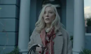 Donna bionda con foulard rosso e cappotto beige, espressione preoccupata. Un'immagine che anticipa un disclaimer serie tv.