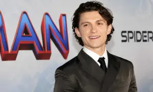 Tom Holland sorride, con indosso un abito scuro. Dietro di lui, il logo di Spider-Man. Chissà quanti anni ha Tom Holland?