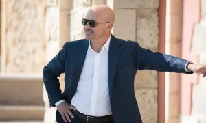 Un uomo calvo con occhiali da sole, giacca blu e camicia bianca, pronto per un'indagine in una delle serie tv poliziesche più avvincenti.