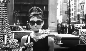Audrey Hepburn, icona di stile, si gode la sua **colazione da Tiffany**, elegante e sofisticata, con un abito nero e gioielli scintillanti.