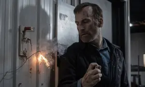 Un uomo con cicatrici sul viso, in un ambiente industriale, mentre un cavo elettrico scintilla. Potrebbe essere una scena del film "Io sono nessuno".