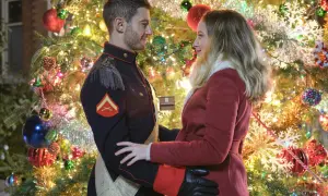 Un uomo in uniforme militare, un principe sotto l'albero di Natale, abbraccia una donna con un cappotto rosso. Le luci scintillanti dell'albero creano un'atmosfera magica.