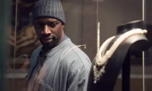 Omar Sy, protagonista di film e programmi TV, osserva con astuzia una collana di perle in una vetrina.