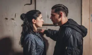 Una donna e un uomo si guardano intensamente. Lei indossa una camicia maculata, lui una giacca con cappuccio. Scena tesa, forse dalla serie "Rosa elettrica".