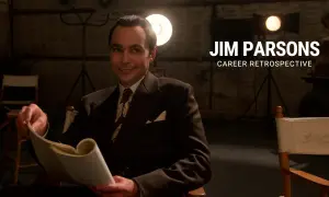 Jim Parsons, in un abito elegante, sfoglia un copione. Un omaggio ai suoi film e programmi TV.