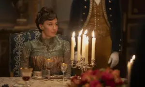 Una donna elegante, in abito d'epoca, siede a tavola durante un sontuoso banchetto, un'immagine che evoca lo sfarzo e le tensioni sociali della Gilded Age.
