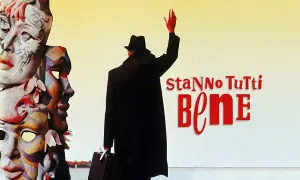 Un uomo con cappello e valigia saluta, circondato da maschere colorate. Il titolo del film "Stanno tutti bene" campeggia in rosso.