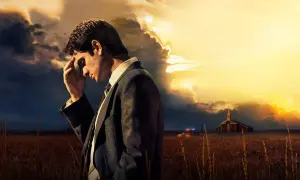 Uomo in abito scuro, con mano sulla fronte, sotto un cielo tempestoso. In lontananza, una chiesa e un'auto della polizia, in nome del cielo.
