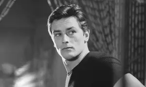 Alain Delon da ragazzo, con sguardo intenso e capelli pettinati all'indietro, indossa una maglia a coste.