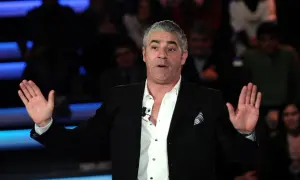 Izzo, attore comico, con le mani aperte sul palco, pronto a far ridere il pubblico.
