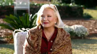 Gena Rowlands, icona dei film d'autore, sorride con un foulard damascato e perle.
