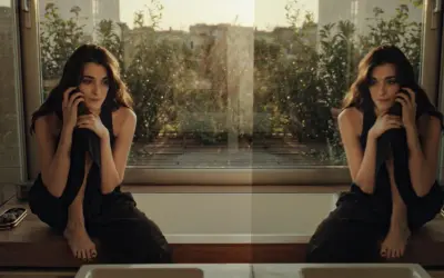 Una donna pensierosa al telefono, seduta su un davanzale con vista su un giardino. Un momento sospeso, forse l'inizio di una breve storia d'amore.