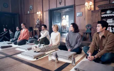 Un gruppo di nove perfetti sconosciuti medita in una stanza di legno, ognuno su un tappetino con coperte piegate.
