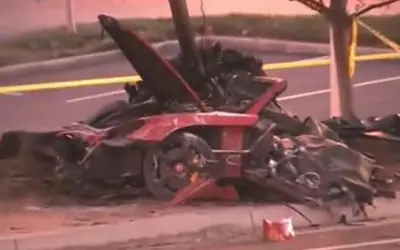 Resti di un'auto rossa distrutta, scena di un tragico incidente che ricorda la paul walker morte. Nastro giallo di delimitazione.