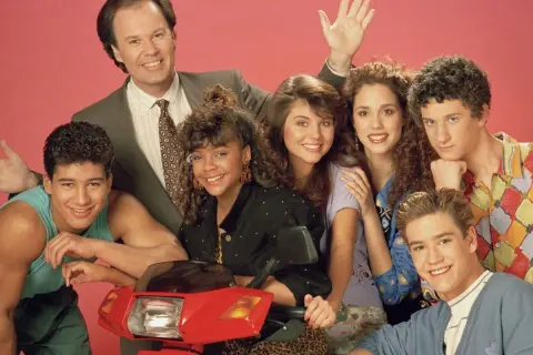 Cast del programma televisivo Bayside School posa sorridente con uno scooter rosso.