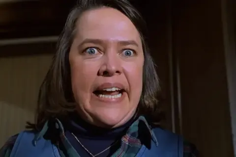 Kathy Bates con occhi sbarrati e bocca aperta in una scena di un film. La sua espressione suggerisce terrore o sorpresa.
