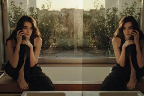 Una donna pensierosa al telefono, seduta su un davanzale con vista su un giardino. Un momento sospeso, forse l'inizio di una breve storia d'amore.