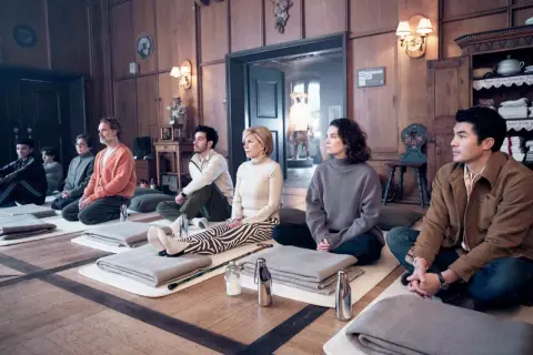 Un gruppo di nove perfetti sconosciuti medita in una stanza di legno, ognuno su un tappetino con coperte piegate.