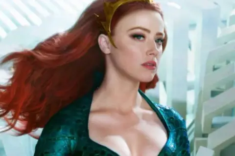 Amber Heard in un film, con lunghi capelli rossi e un diadema dorato, indossa un abito verde acqua.