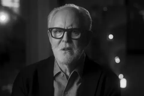 Primo piano in bianco e nero di John Lithgow con occhiali, che riflette sulla sua carriera nei film e programmi TV.