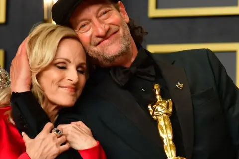 Il cast di coda, con i segni del cuore, celebra un momento d'oro. L'Oscar brilla, simbolo di un amore che supera ogni barriera.