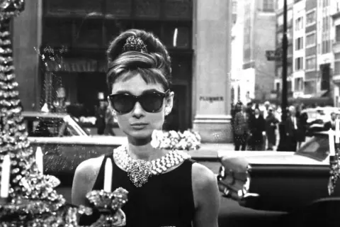 Audrey Hepburn, icona di stile, si gode la sua **colazione da Tiffany**, elegante e sofisticata, con un abito nero e gioielli scintillanti.