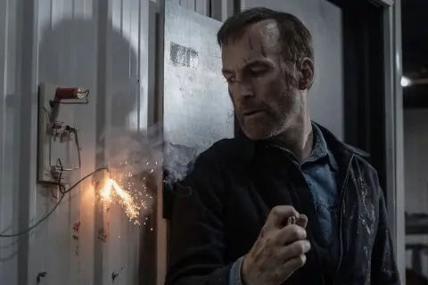 Un uomo con cicatrici sul viso, in un ambiente industriale, mentre un cavo elettrico scintilla. Potrebbe essere una scena del film "Io sono nessuno".