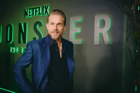 Charlie Hunnam, protagonista di film e programmi TV, posa con un sorriso davanti al logo Netflix.