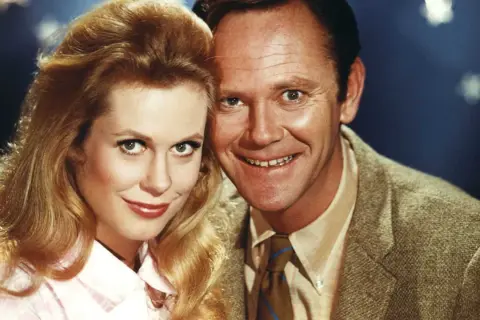 Il cast di Vita da strega: Elizabeth Montgomery e Dick York sorridono vicini, con lei che indossa una camicetta rosa e lui una giacca di tweed.