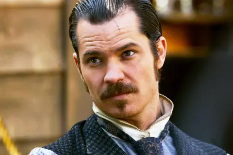 Timothy Olyphant, con cicatrice sulla fronte, baffi e basette, in abiti d'epoca, un volto iconico dei suoi film e programmi TV.