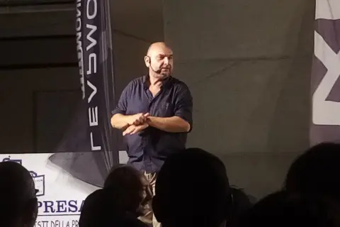 Giovanni Cacioppo, con un microfono all'orecchio, parla a un pubblico. La sua storia sulla malattia ispira.