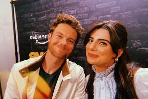 Jack Quaid sorride con la sua fidanzata, una foto scattata davanti a uno sfondo con il logo di Amazon.