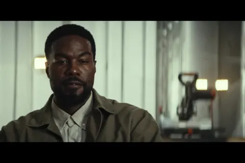 Primo piano di un uomo con barba, in abiti casual, in una scena della serie TV "Man on Fire".