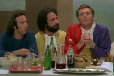 Il cast de "Il Pap'occhio" a tavola, tra bottiglie di vino e pane.