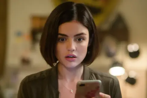 Lucy Hale, protagonista di film e programmi TV, guarda sorpresa il suo telefono.
