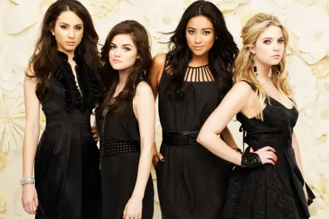 Il cast di Pretty Little Liars posa in abiti eleganti neri su uno sfondo floreale.