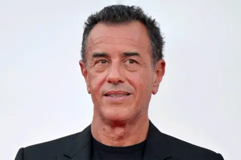 Matteo Garrone, regista italiano, con un sorriso enigmatico. La sua carriera è segnata da film potenti e visivamente sorprendenti.