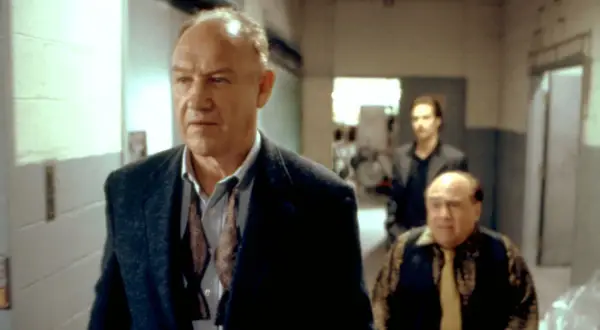 Gene Hackman in un film, cammina con altri due uomini in un corridoio.