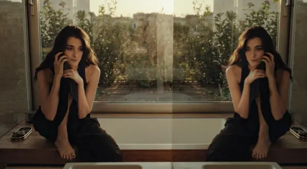 Una donna pensierosa al telefono, seduta su un davanzale con vista su un giardino. Un momento sospeso, forse l'inizio di una breve storia d'amore.