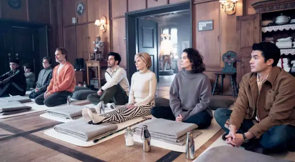 Un gruppo di nove perfetti sconosciuti medita in una stanza di legno, ognuno su un tappetino con coperte piegate.