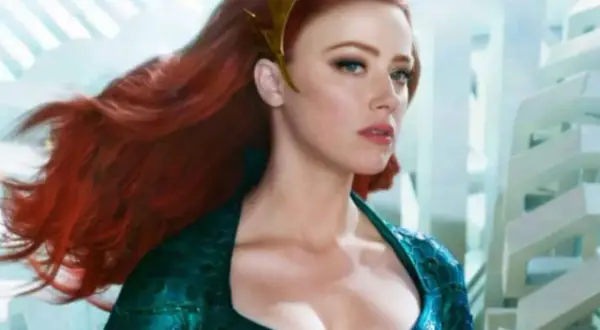 Amber Heard in un film, con lunghi capelli rossi e un diadema dorato, indossa un abito verde acqua.