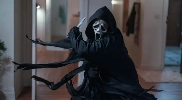 Ghostface, icona del film di Scream, brandisce un coltello con la sua maschera spettrale e il mantello svolazzante.