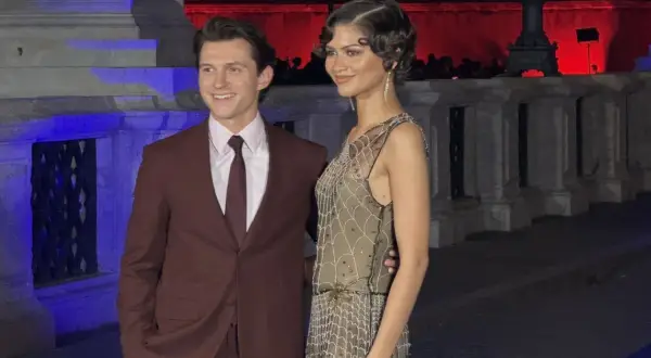 Tom Holland e Zendaya, una coppia iconica, sorridono alla telecamera. Lui indossa un completo bordeaux, lei un abito scintillante.