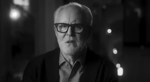 Primo piano in bianco e nero di John Lithgow con occhiali, che riflette sulla sua carriera nei film e programmi TV.