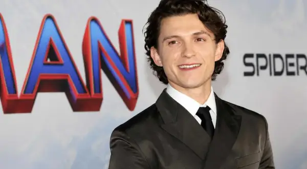 Tom Holland sorride, con indosso un abito scuro. Dietro di lui, il logo di Spider-Man. Chissà quanti anni ha Tom Holland?