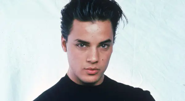 Ritratto di Nick Kamen, un giovane uomo con capelli scuri pettinati all'indietro e un maglione nero. La sua espressione è seria, mentre si riflette sulla sua **malattia**.
