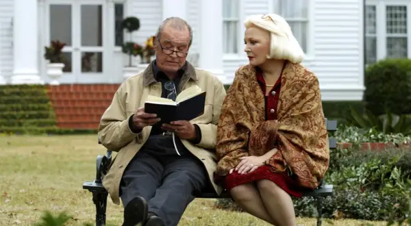 Il cast di "Le pagine della nostra vita" seduto su una panchina, un uomo legge un libro, una donna lo ascolta con attenzione.