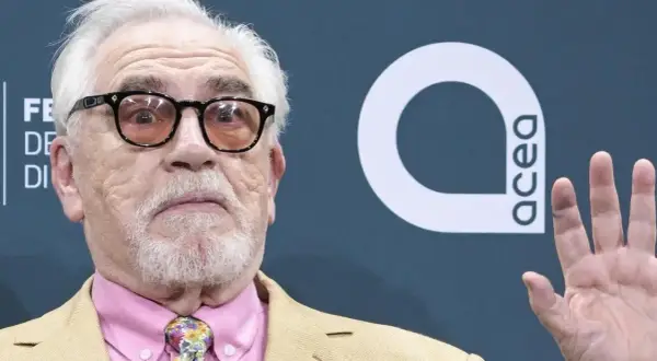 Brian Cox, noto per i suoi film e programmi TV, con occhiali e cravatta colorata.